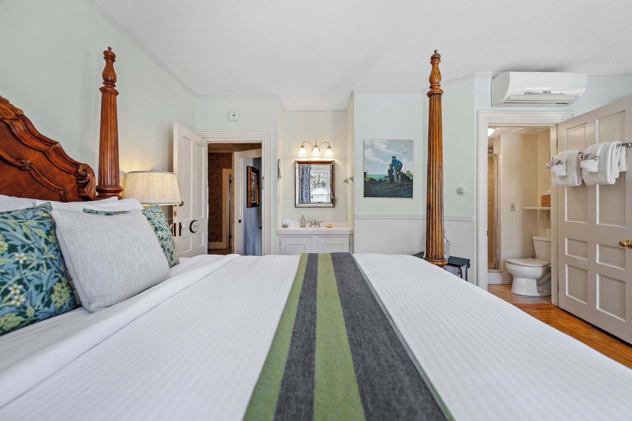Una habitación de hotel con una cama grande, cabecera de madera, tocador con espejo y baño con inodoro y toallero.