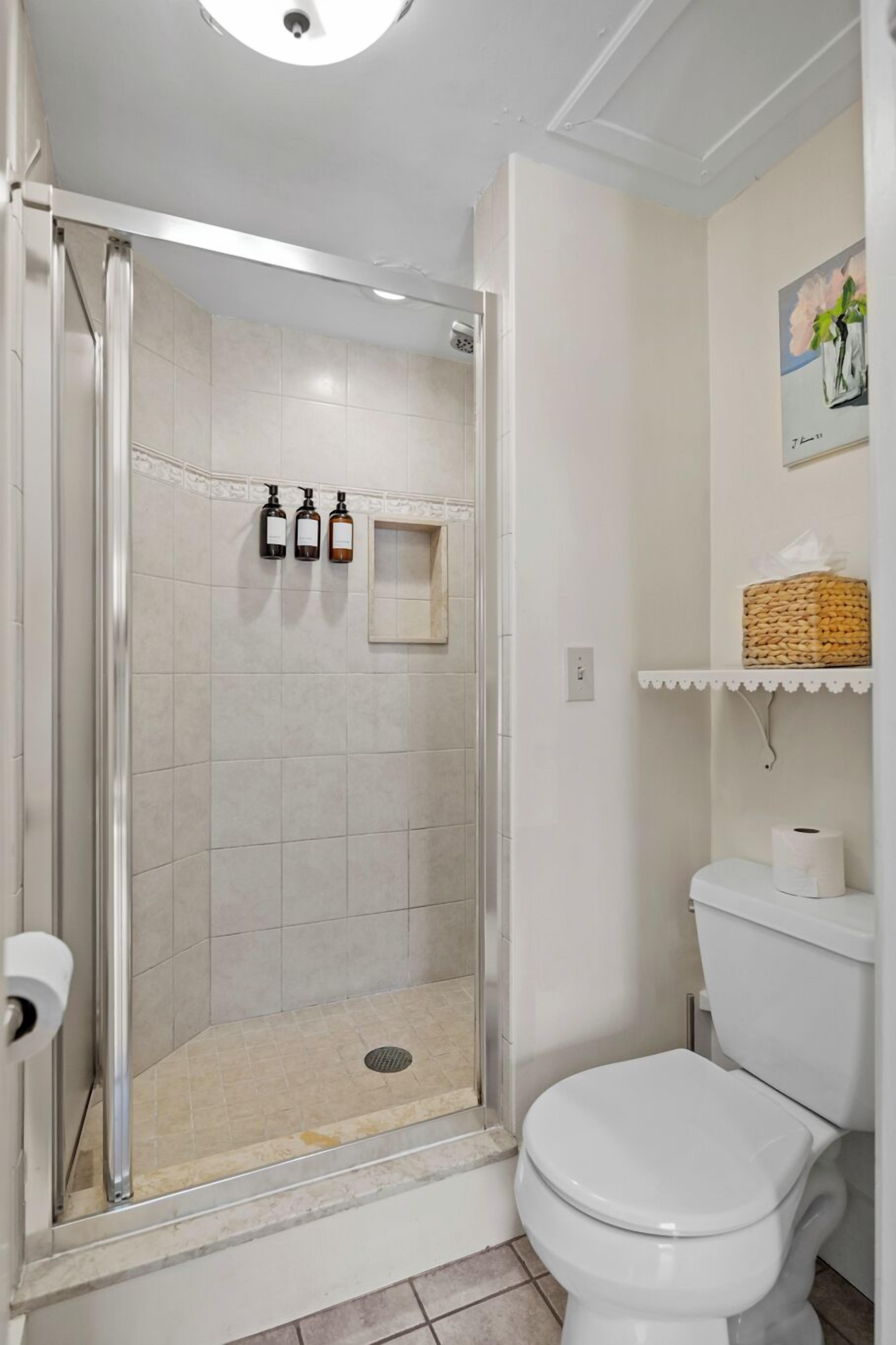 Un baño con ducha, inodoro y repisa con artículos de aseo.