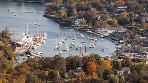 A marina with numerous boats docked, surrounded by residential buildings and autumn foliage. - Hartstone Inn (Camden)