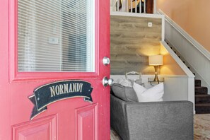 A red door with a sign reading "Normandy" and a grey couch in the background.