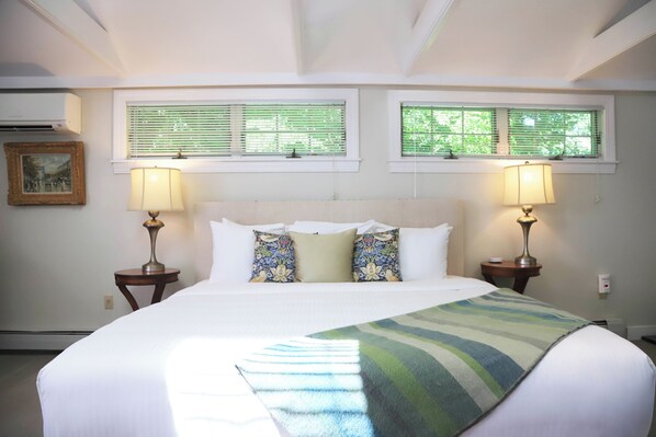 A hotel room with a large bed, two bedside tables with lamps, a window with blinds, and a picture on the wall.
