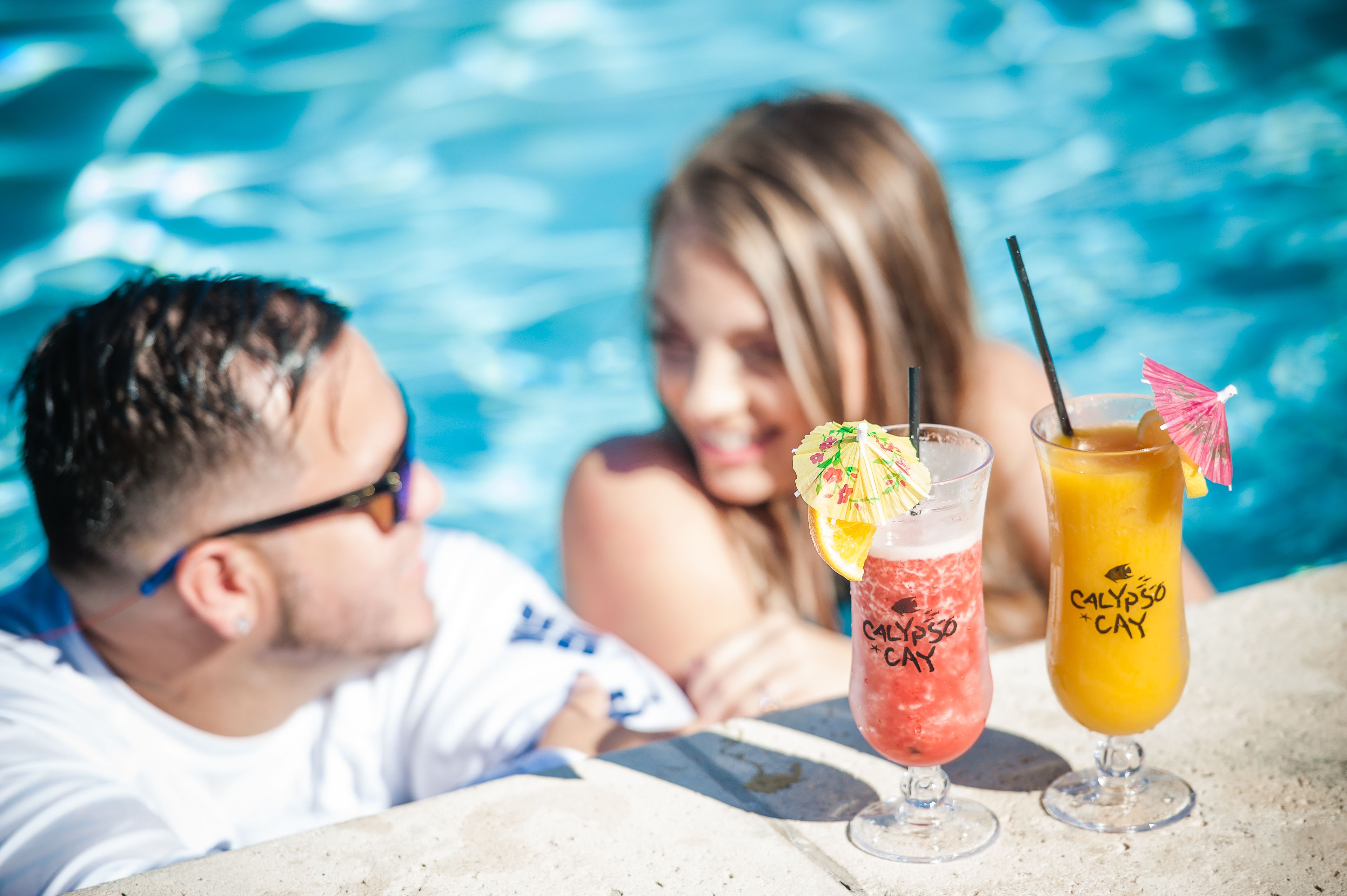 A poolside setting with two drinks labeled 'CALYPSO CAY' and 'CALYPSO CAY + CAY' with straws and garnishes.