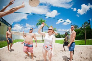 Um grupo de pessoas jogando voleibol de praia em uma quadra arenosa com uma rede.