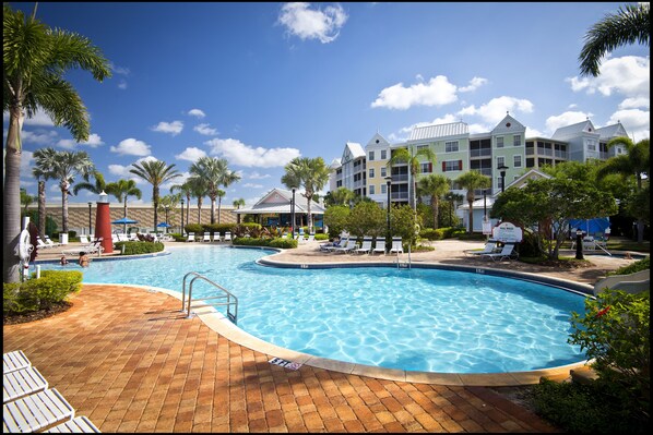 A swimming pool with lounge chairs, palm trees, and a hotel building in the background.