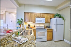 A kitchen with granite countertops, wooden cabinets, a white refrigerator, a microwave, an oven, and a sink.