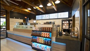 Interior de una cafetería con una exhibición de productos de café, una barra con un menú y una sección de panadería.