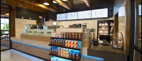 Interieur van een koffiebar met een presentatie van koffieproducten, een toonbank met een menubord en een bakkerijgedeelte.