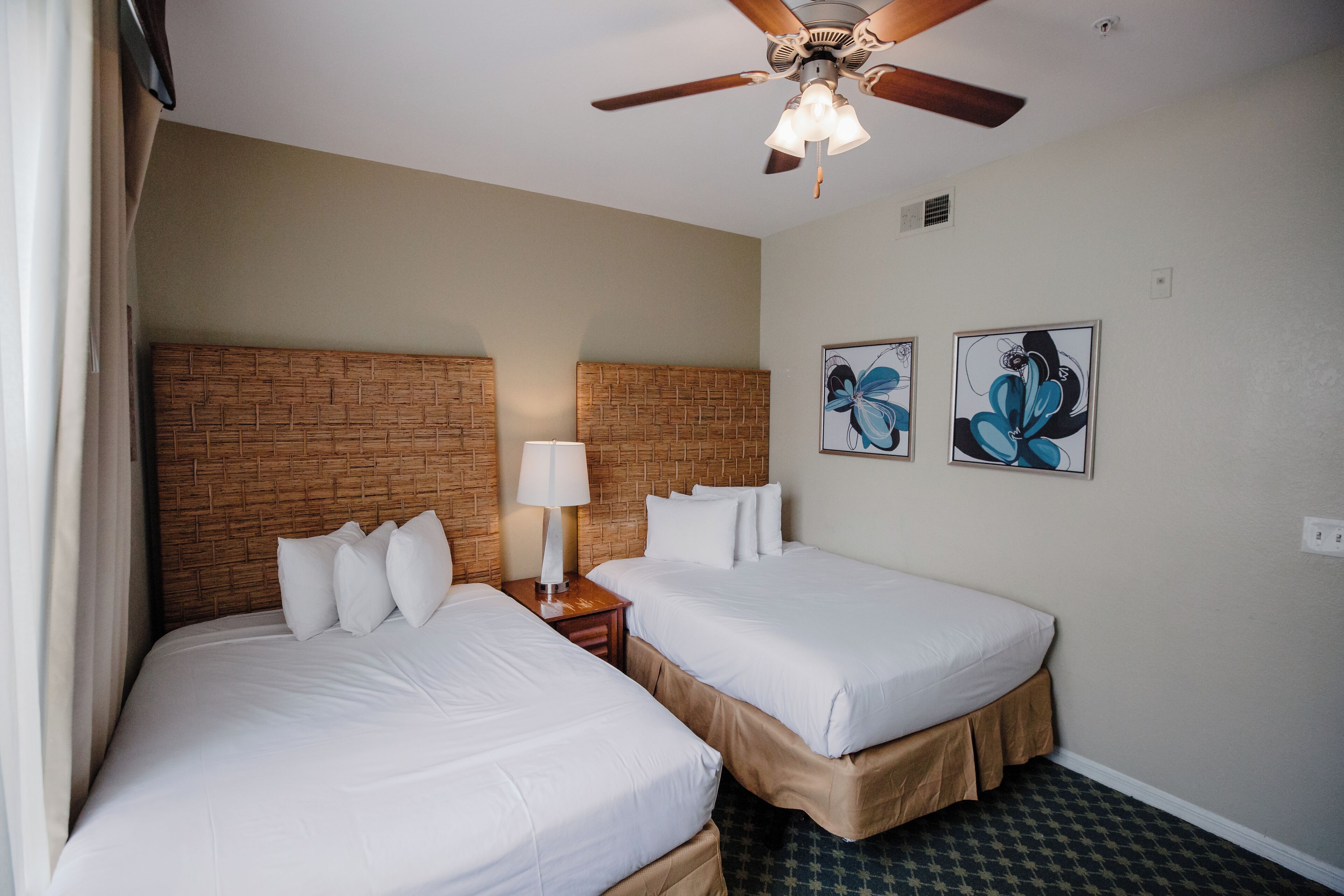 Ein Hotelzimmer mit zwei Betten, einem Deckenventilator und Bildern an der Wand.