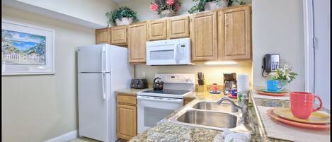 A kitchen with wooden cabinets, a white refrigerator, a microwave, a stove, and a sink.