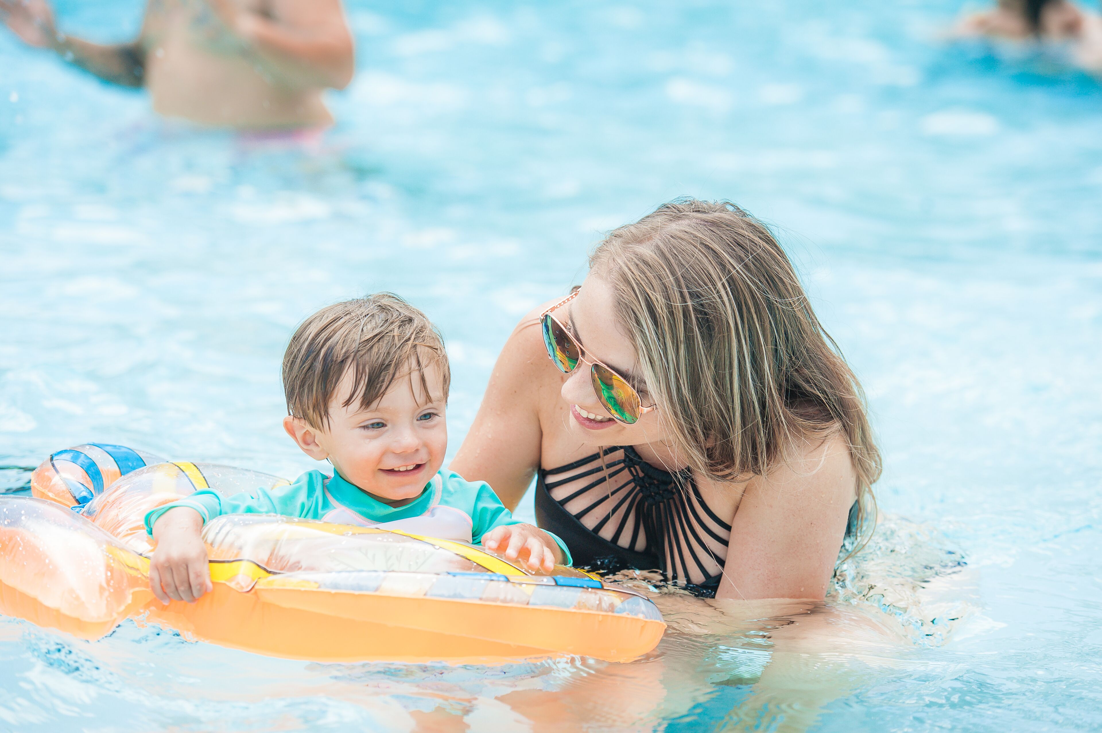 Una piscina con agua cristalina y un niño sobre un flotador.