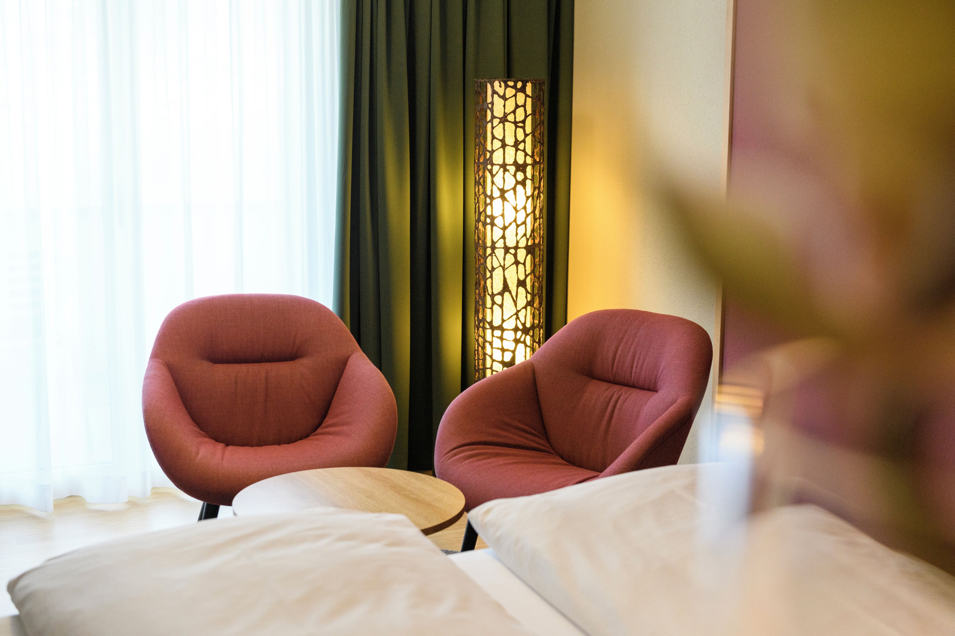 Ein Hotelzimmer mit zwei roten Sesseln, einem Holznachttisch und einer dekorativen Lampe.
