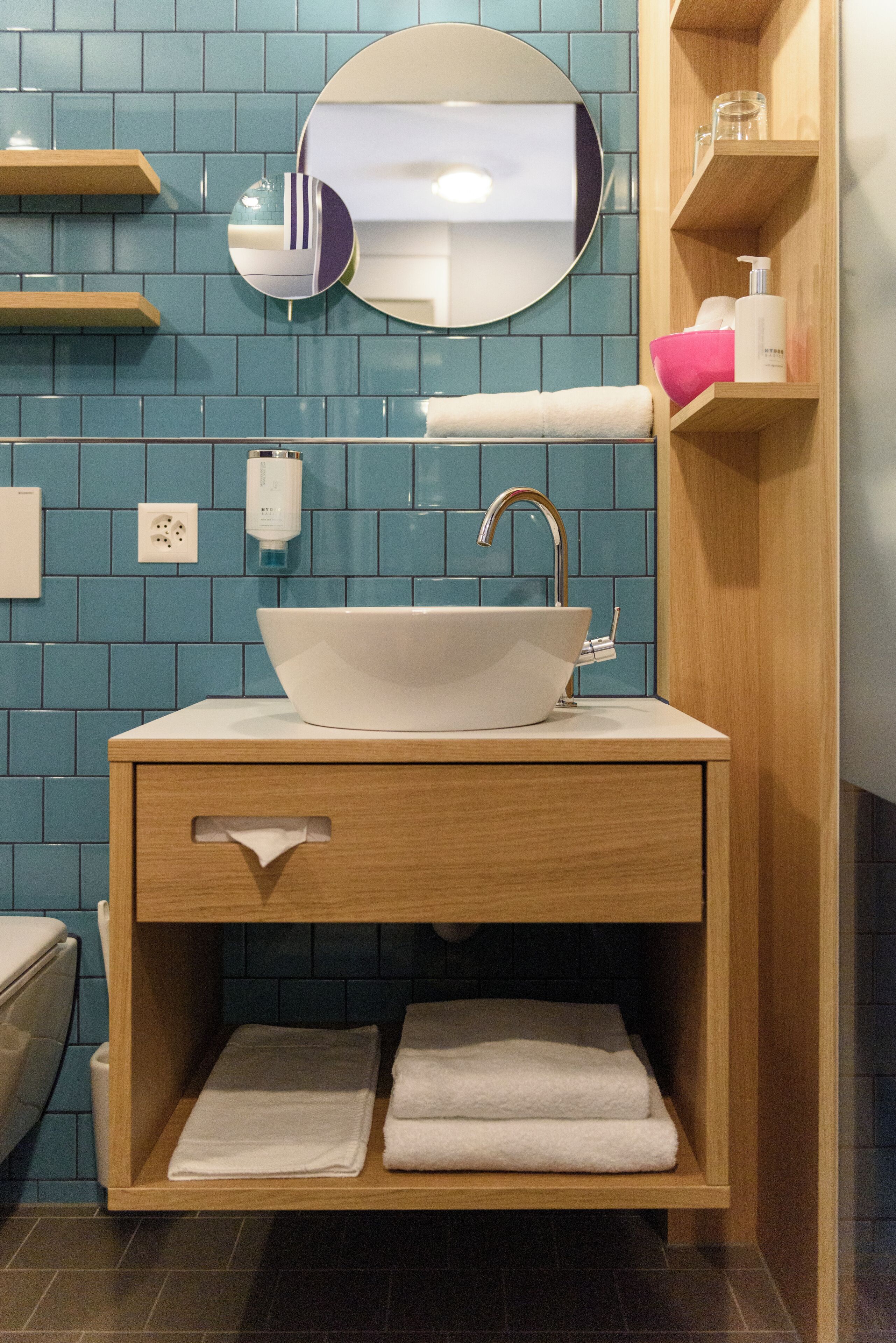 A bathroom with a white sink, wooden vanity, and blue tiled walls.