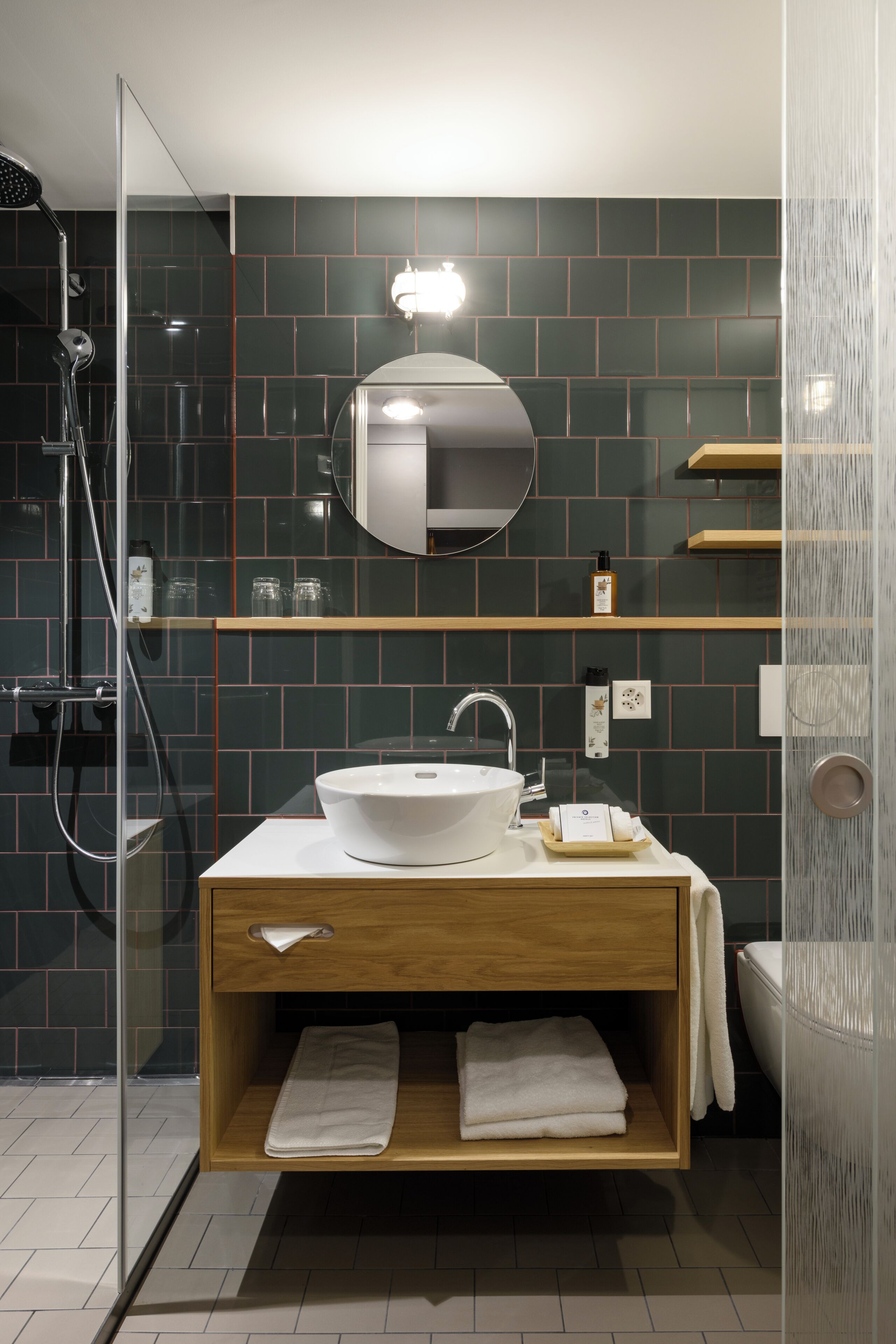 Een moderne badkamer met een douchecabine van glas, een witte wastafel en een houten opbergmeubel.