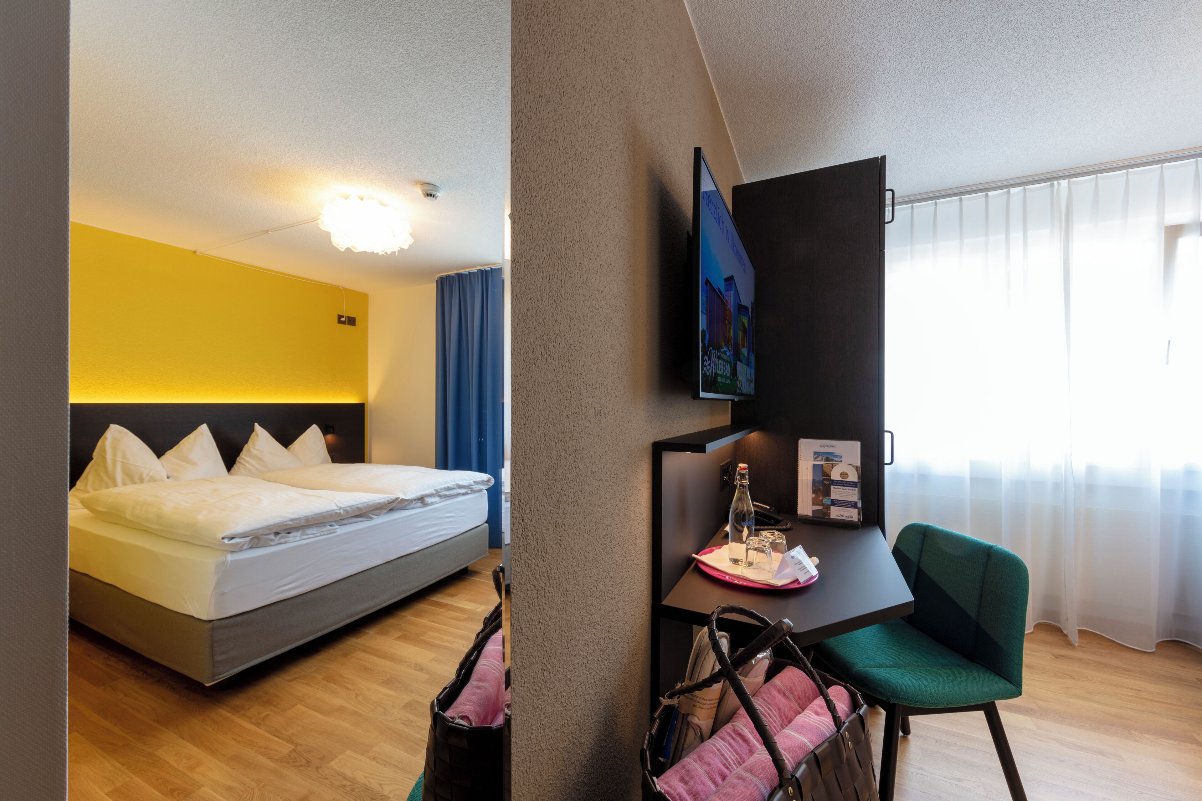 Ein Hotelzimmer mit Bett, Schreibtisch, Stuhl, Fernseher und einem Fenster mit Vorhängen.