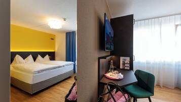 Ein Hotelzimmer mit Bett, Schreibtisch, Stuhl, Fernseher und einem Fenster mit Vorhängen.