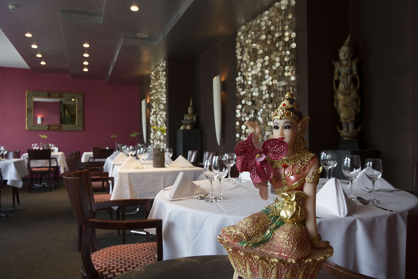 Um restaurante com mesas preparadas para refeições, uma estátua na parede e um adorno decorativo na parede.