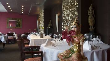 Um restaurante com mesas preparadas para refeições, uma estátua na parede e um adorno decorativo na parede.