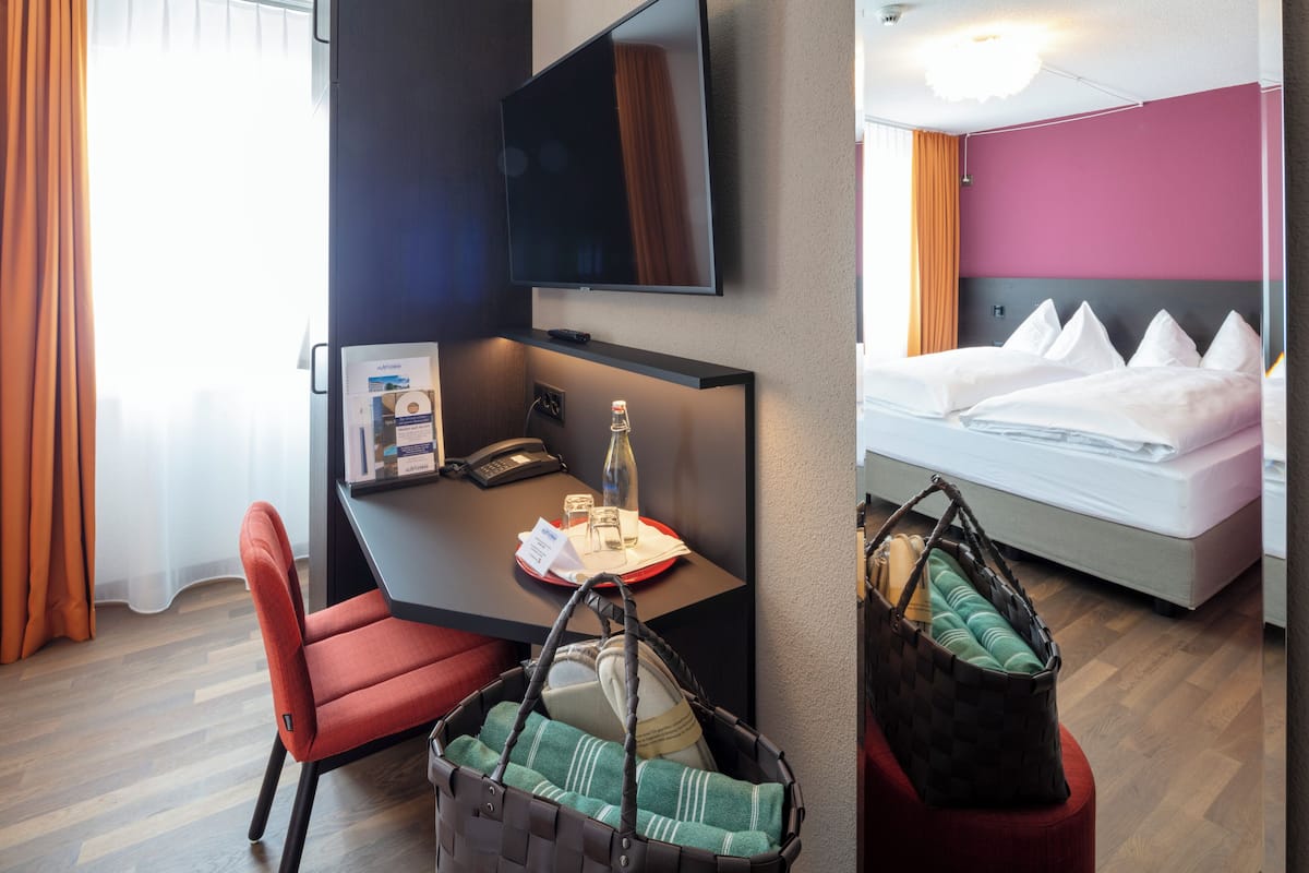 A hotel room with a desk, chair, bed, and a TV mounted on the wall.
