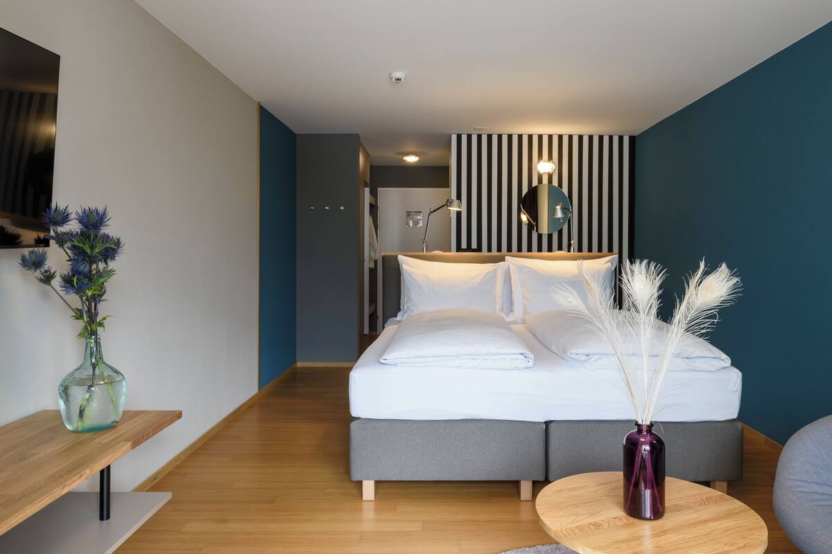 A modern hotel room with a bed, bedside table, and a vase with pampas grass.