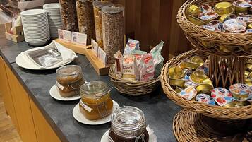 A buffet counter with various food items, including jars of preserves and packaged snacks.
