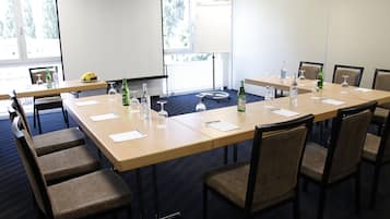 A conference room with a large table, chairs, a projector screen, and a window with a view of trees.