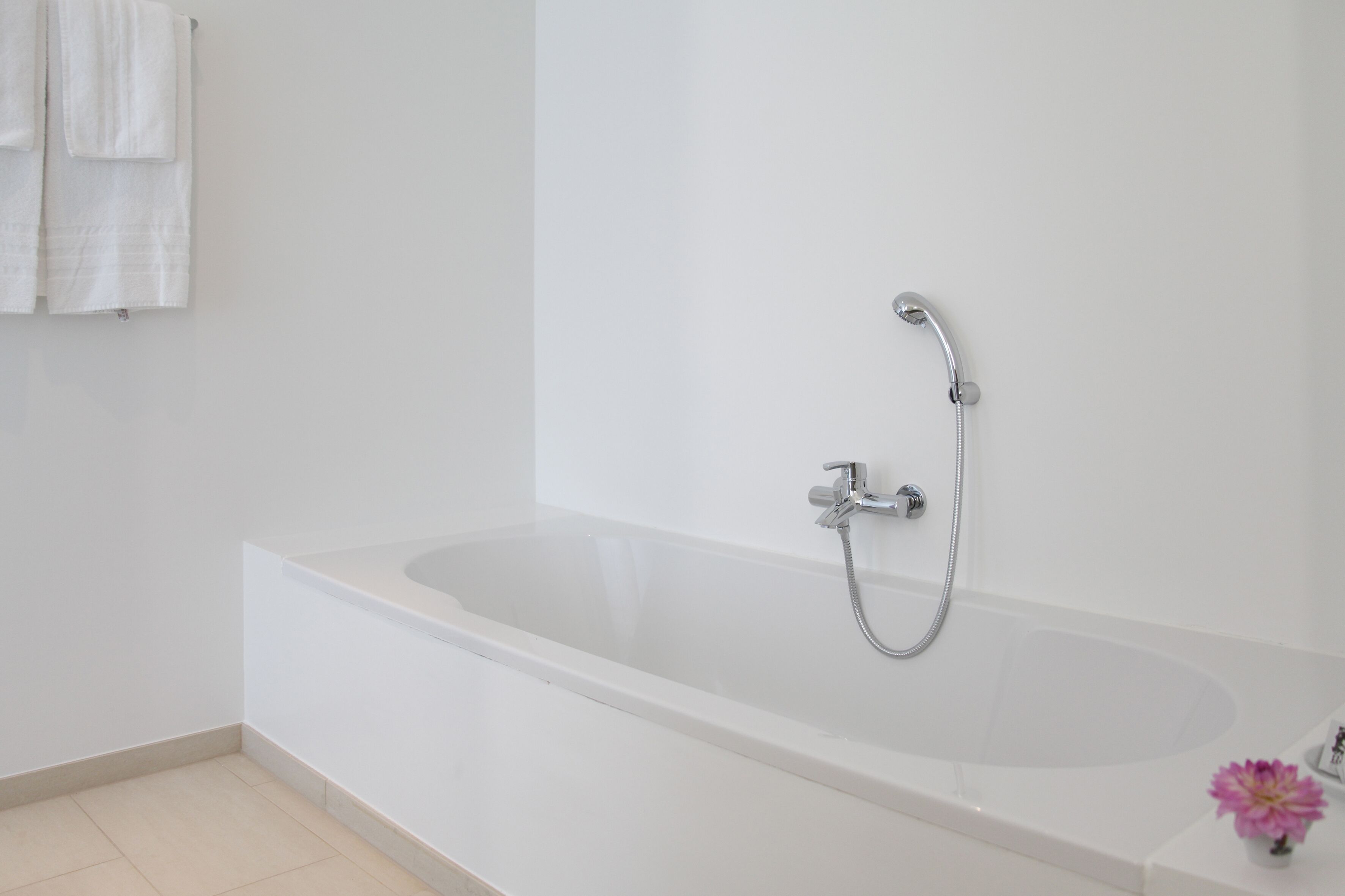 Une salle de bain moderne avec une baignoire blanche, une pomme de douche et un petit vase avec une fleur.