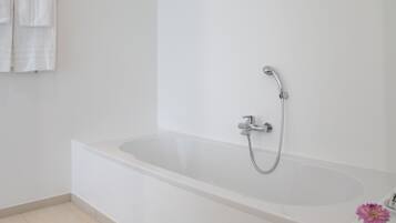 Une salle de bain moderne avec une baignoire blanche, une pomme de douche et un petit vase avec une fleur.
