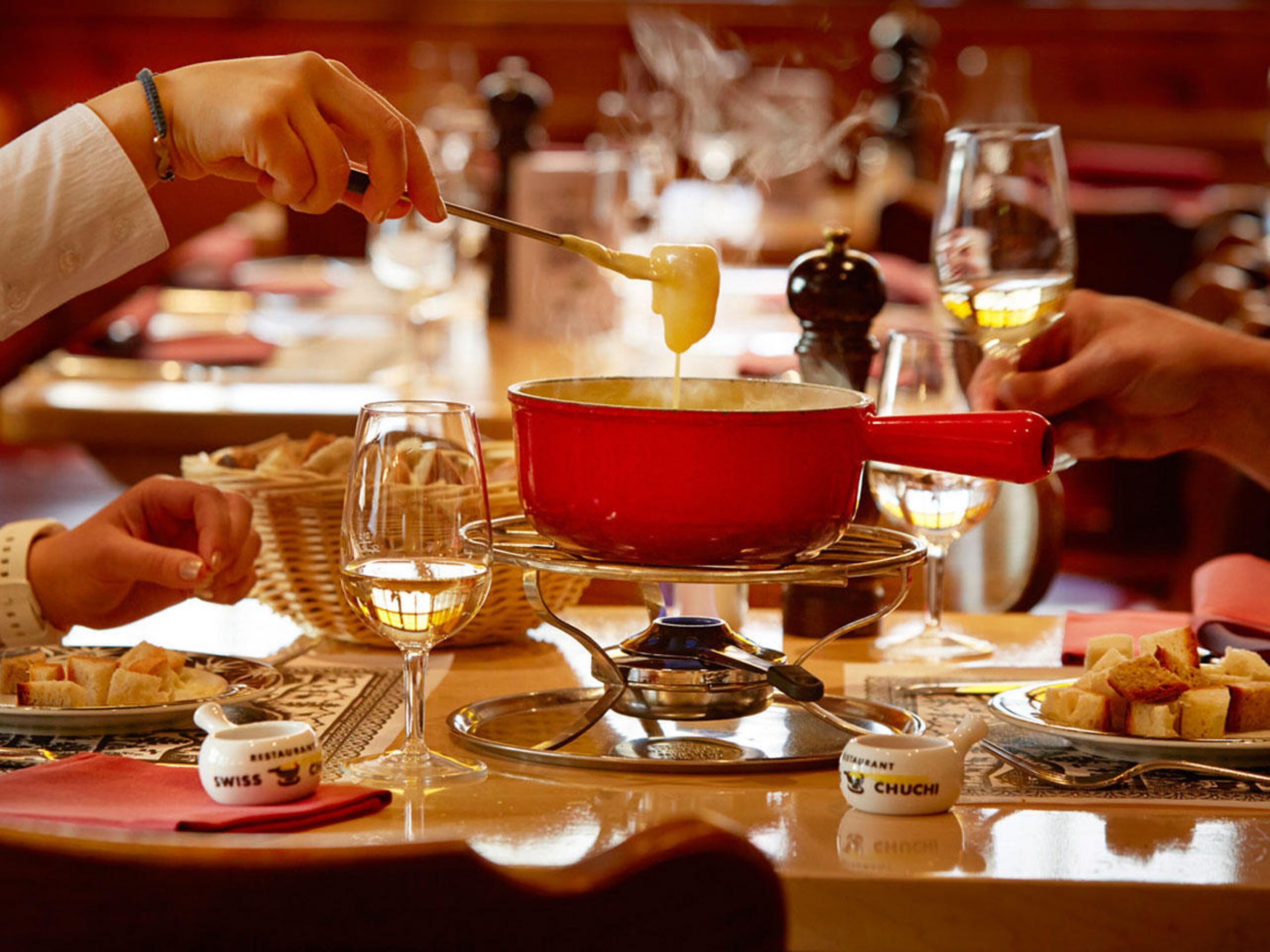 Una mesa de comedor con una olla roja de sopa, copas de vino y platos de comida.