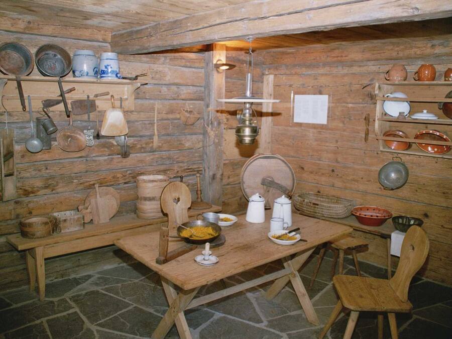 Una habitación rústica de madera con estantes que exhiben diversos utensilios y utensilios de cocina. Una mesa de madera con sillas se encuentra en el centro.