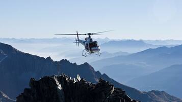 A helicopter flying over a mountainous landscape with rocky terrain and a cross on a peak.