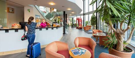 A modern hotel lobby with a reception desk, seating area, and a staircase.