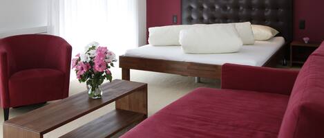 A modern bedroom with a wooden bed, red upholstered chairs, a wooden coffee table, and a vase of flowers.