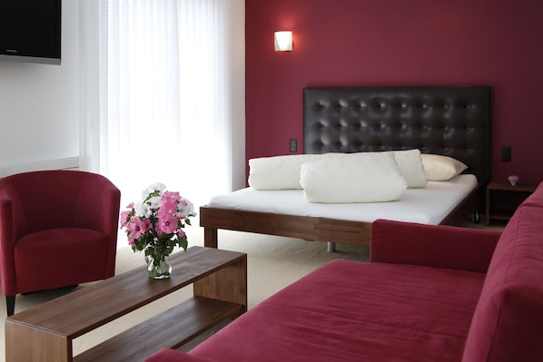 A modern bedroom with a wooden bed, red upholstered chairs, a wooden coffee table, and a vase of flowers.