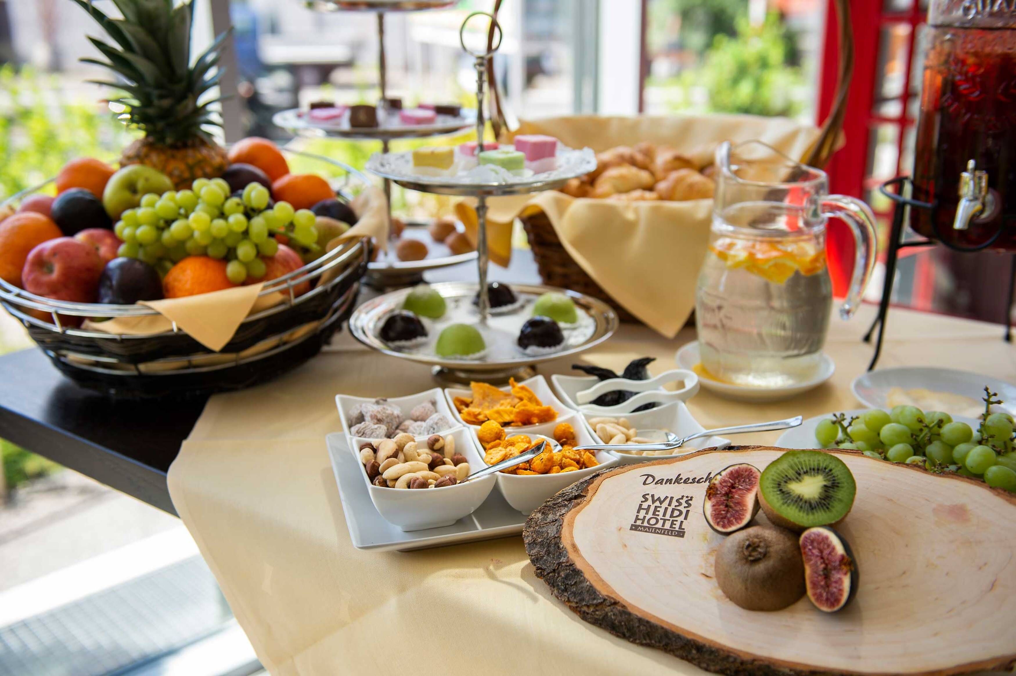 A buffet table with various fruits, pastries, and a drink dispenser.