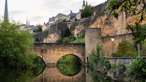 A historic stone bridge with circular openings over a river, leading to a fortified city with medieval architecture. - Sofitel Luxembourg Le Grand Ducal (Luxembourg City)