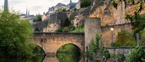 A historic stone bridge with circular openings over a river, leading to a fortified city with medieval architecture.