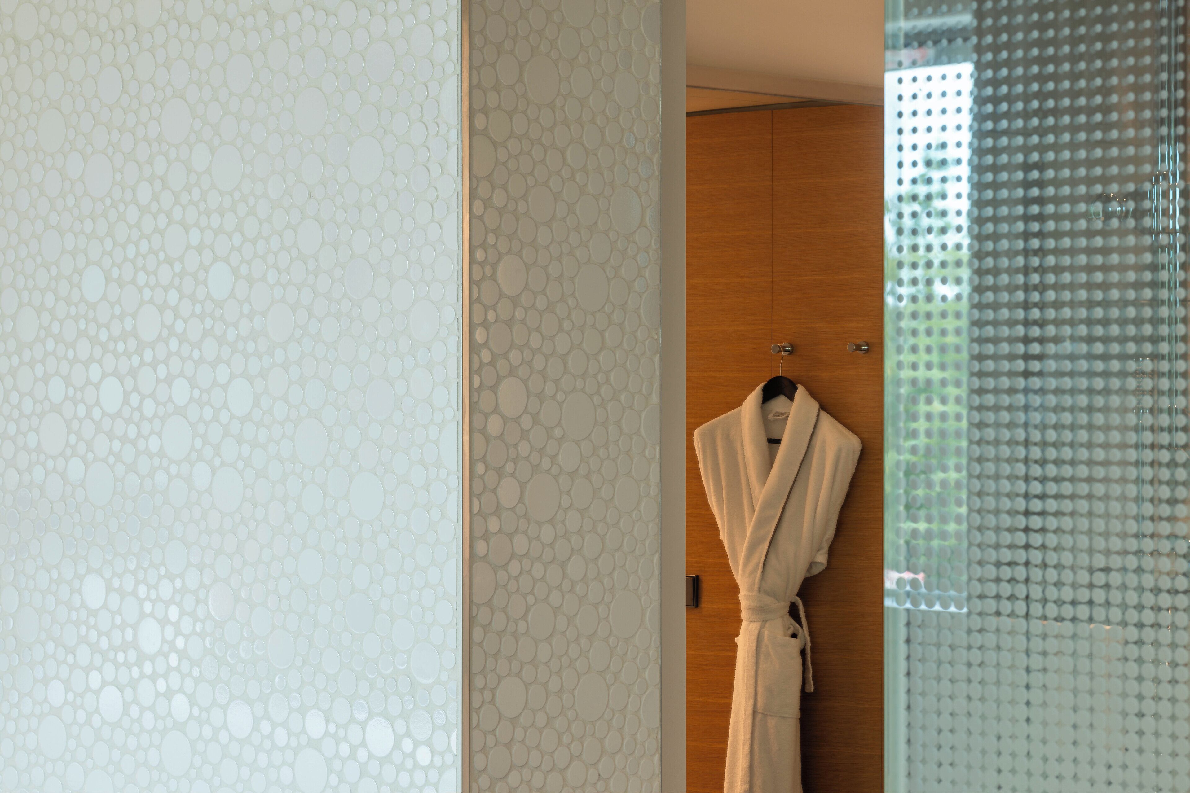 A bathroom with a patterned wall, a wooden door, and a white robe hanging on a hook.