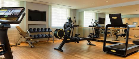 Un gimnasio con máquinas de cardio, mancuernas y una pantalla de televisión.