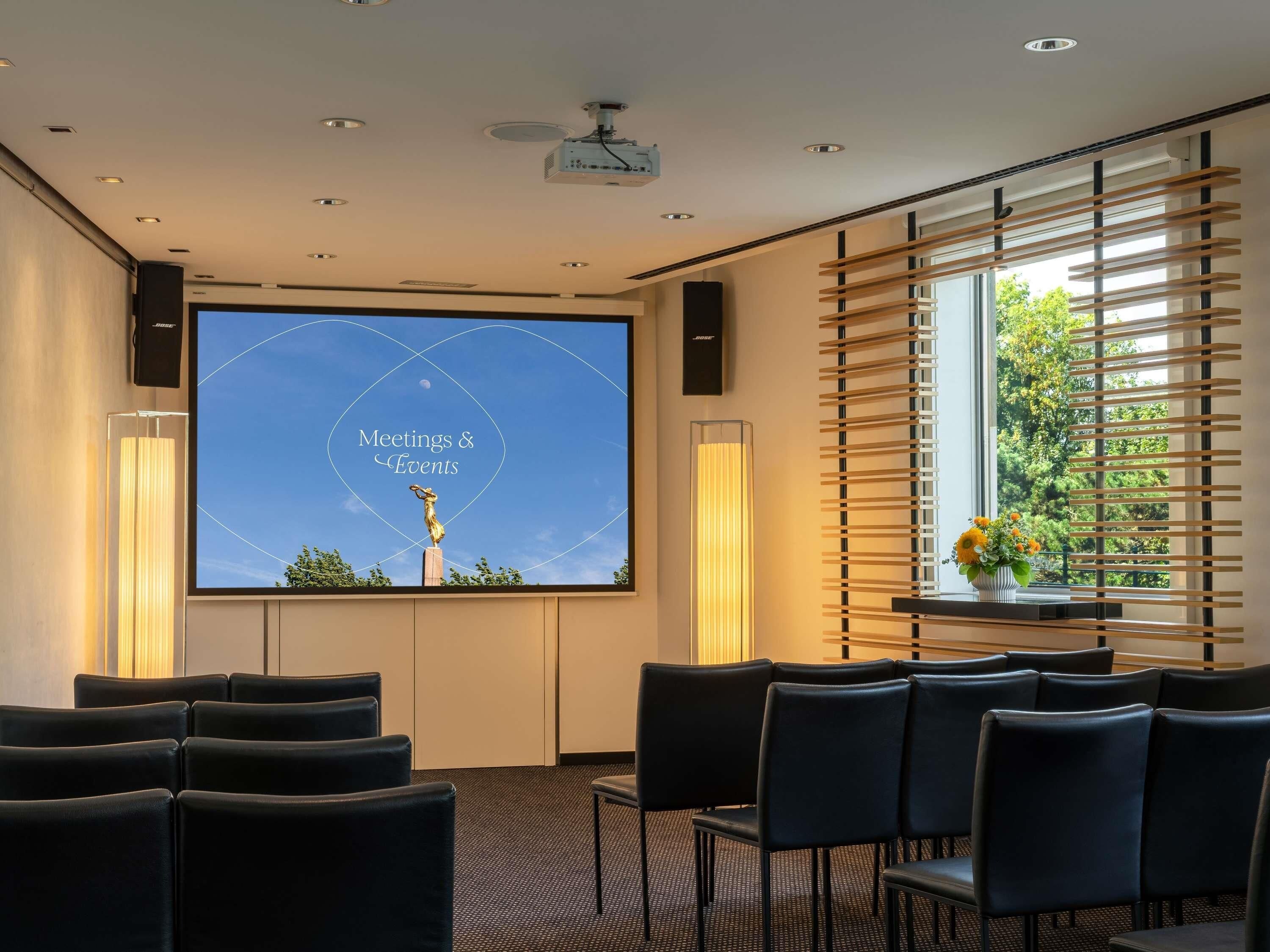 A conference room with a projector screen displaying 'Meetings & Events,' a statue, and a window with blinds.