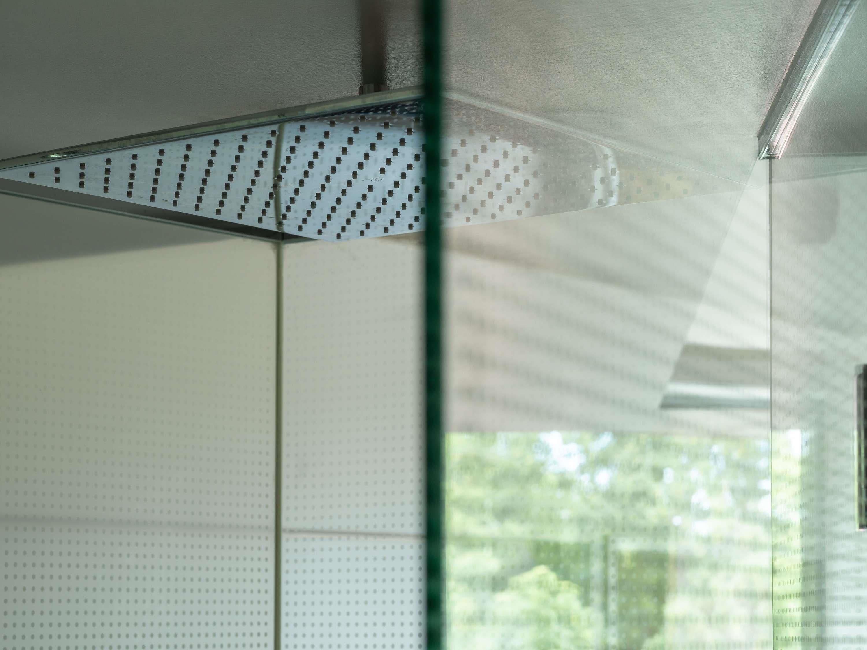 A room with a ceiling vent, a window with a view of greenery, and a wall with a dotted pattern.
