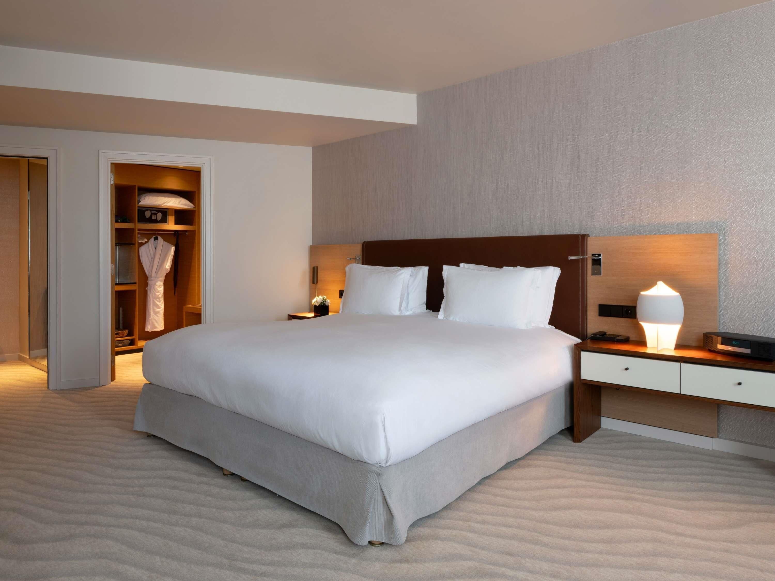 A hotel room with a large bed, bedside tables, a nightstand, a lamp, a wardrobe, and a mirror.