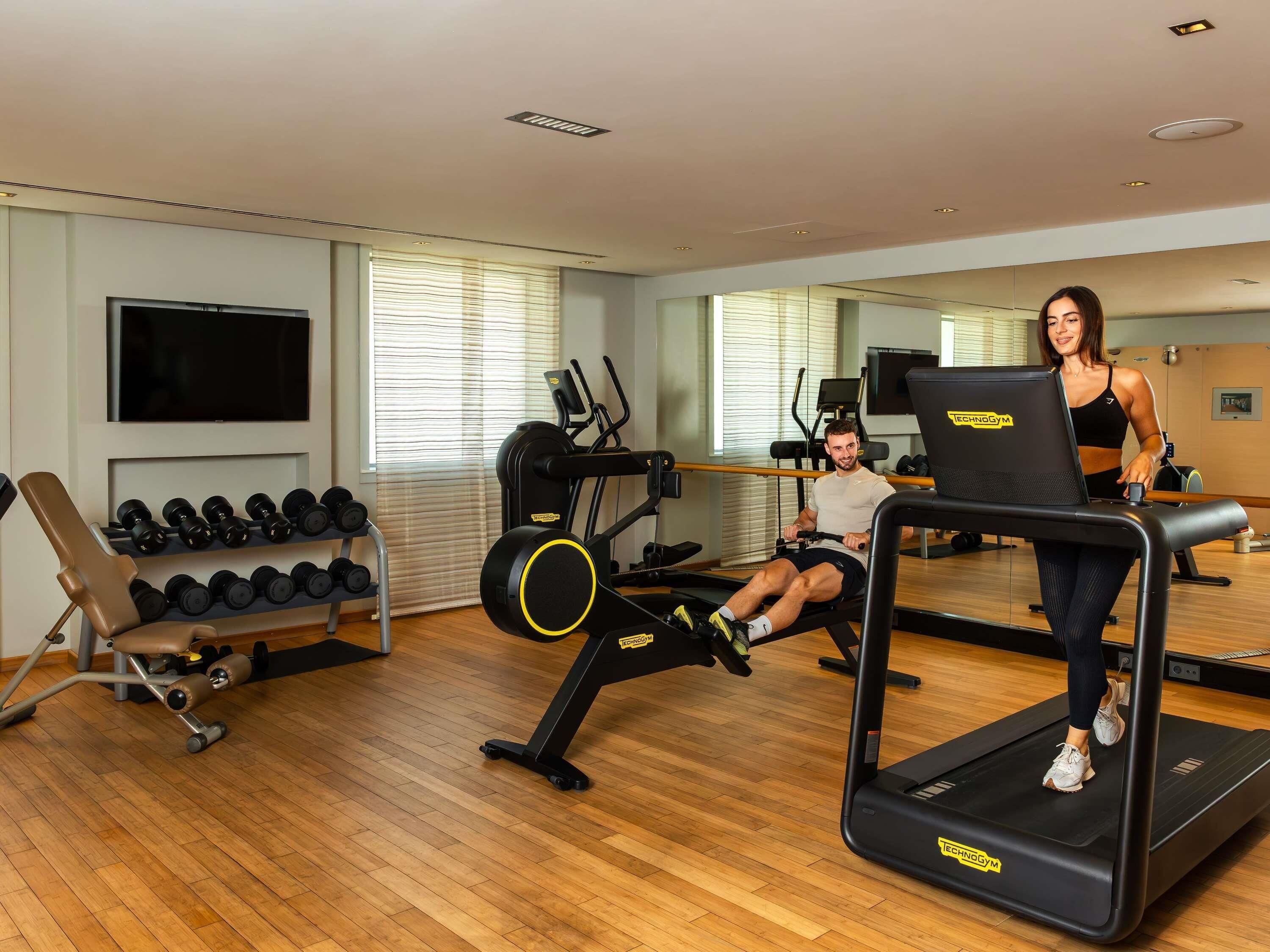 A gym with cardio machines, dumbbells, and a TV.