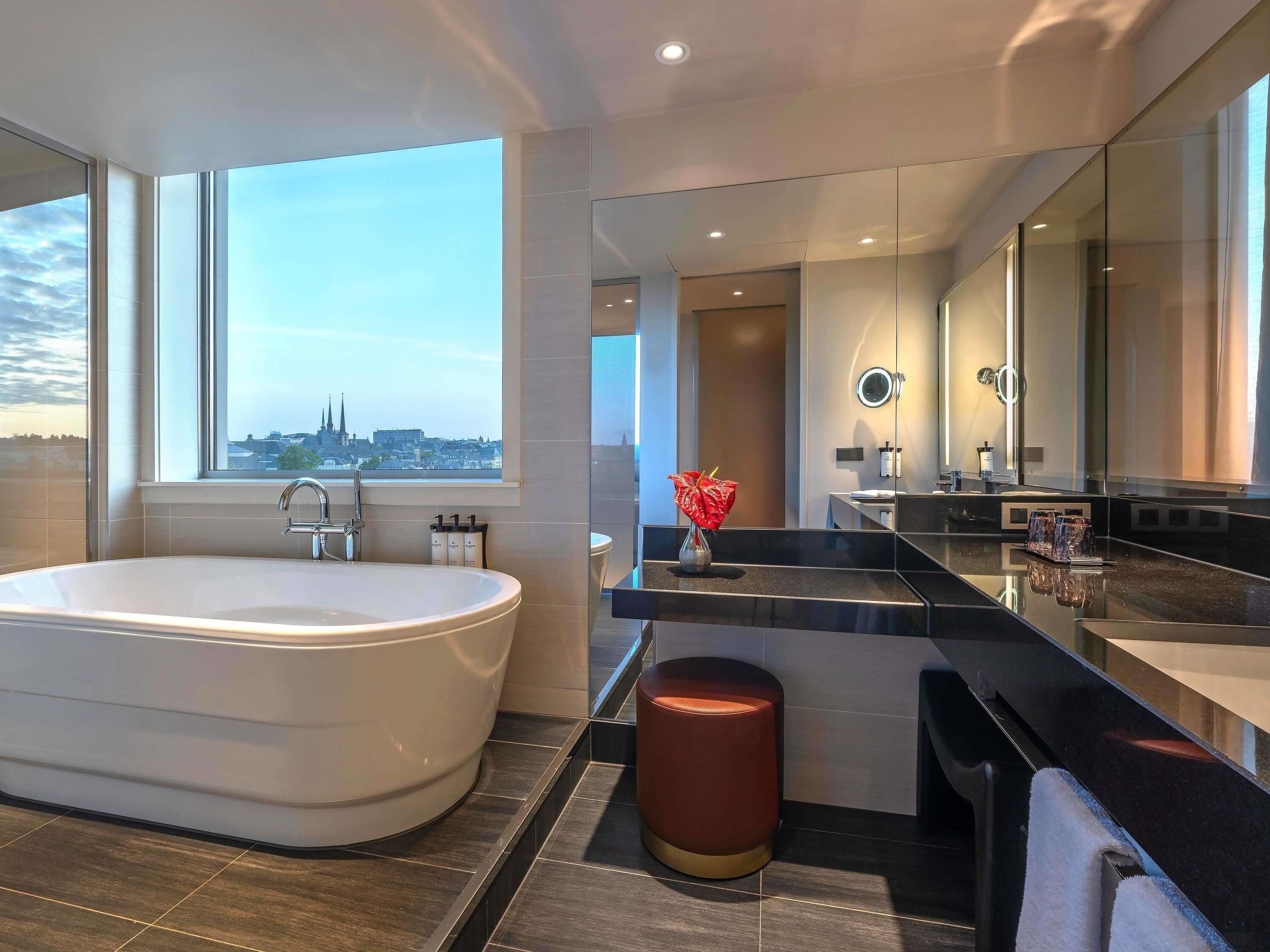 A modern bathroom with a large bathtub, a vanity with a mirror, and a view of a cityscape.