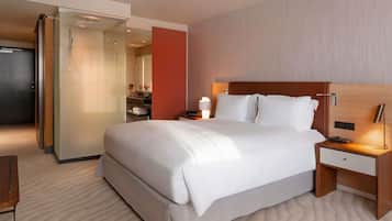 Ein Hotelzimmer mit einem großen Bett, einem Nachttisch mit Lampe, einer Dusche mit Glastrennwand und einem Badezimmer mit Spiegel und Handtuchhalter.