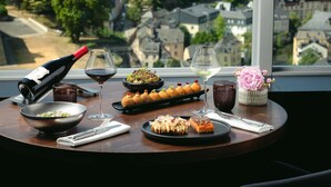 A table with food and drinks, a bottle of wine, and a view of buildings through a window. - Sofitel Luxembourg Le Grand Ducal (Luxembourg City)