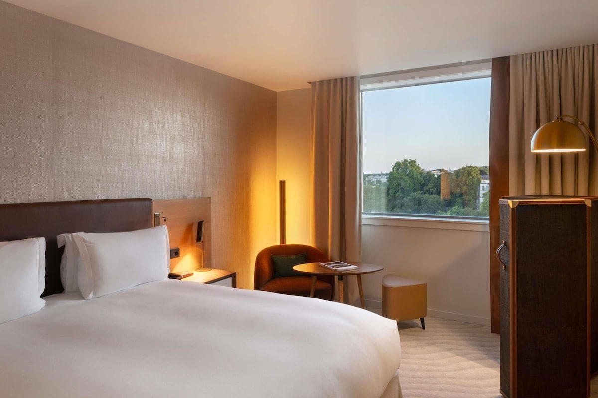 Ein Hotelzimmer mit einem großen Bett, einem Schreibtisch, einem Stuhl, einem kleinen Tisch, einer Lampe und einem Kleiderschrank.