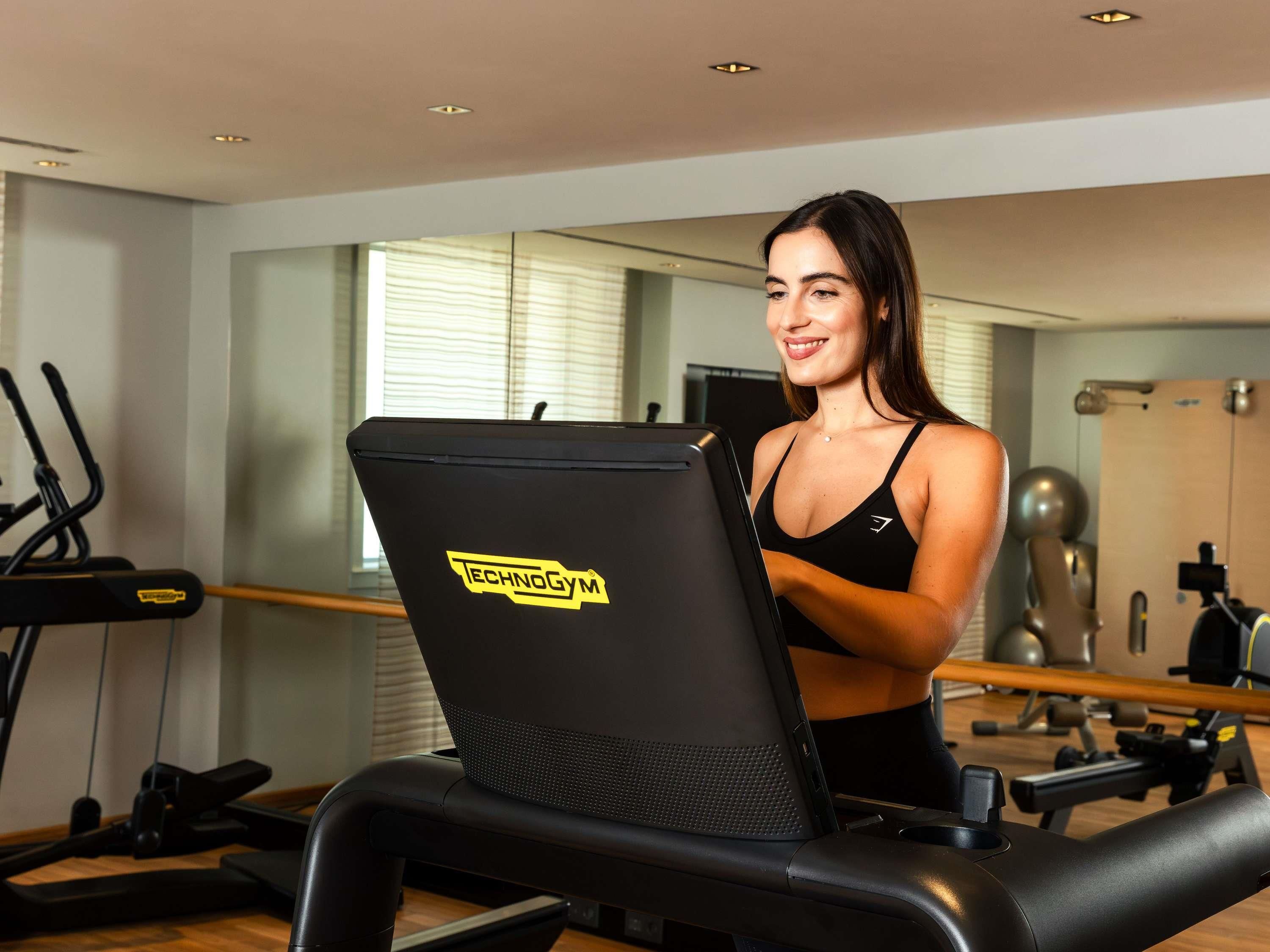 Een sportschool met een loopband, een spiegel en fitnessapparatuur.