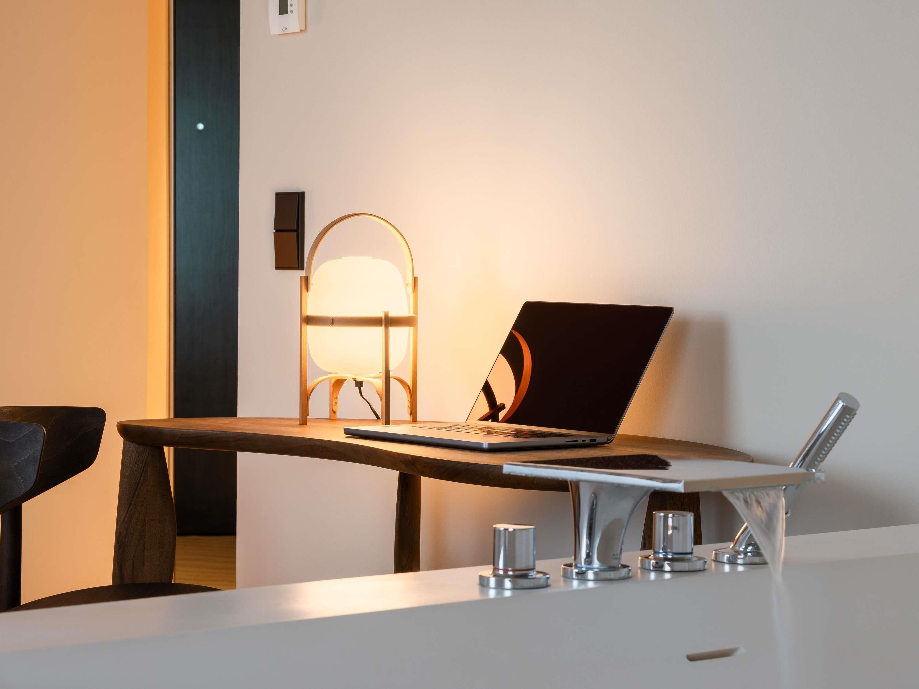 Un bureau moderne avec un ordinateur portable, une lampe et un verre d’eau.