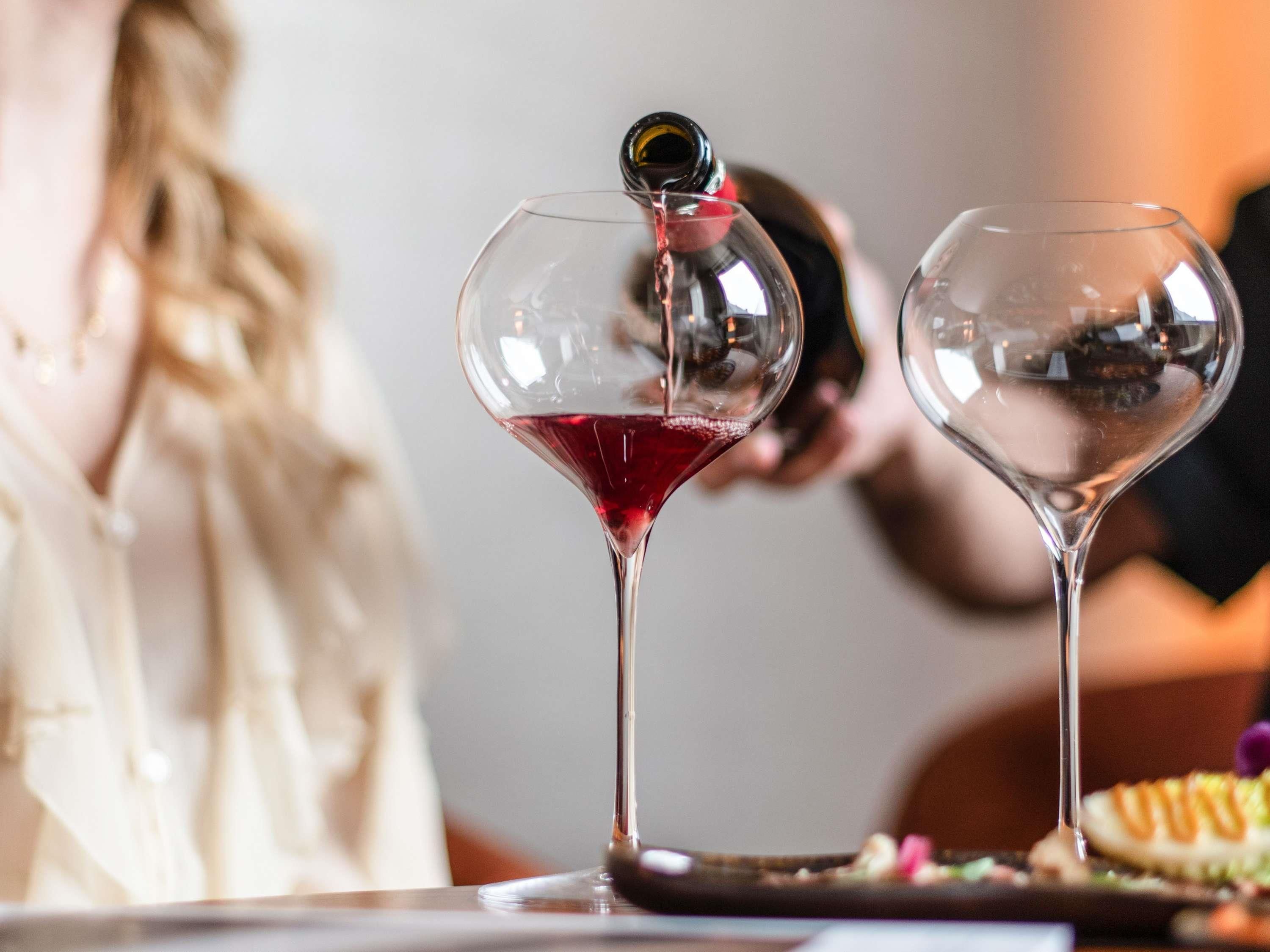 Two wine glasses on a table, one with a red liquid being poured into it.