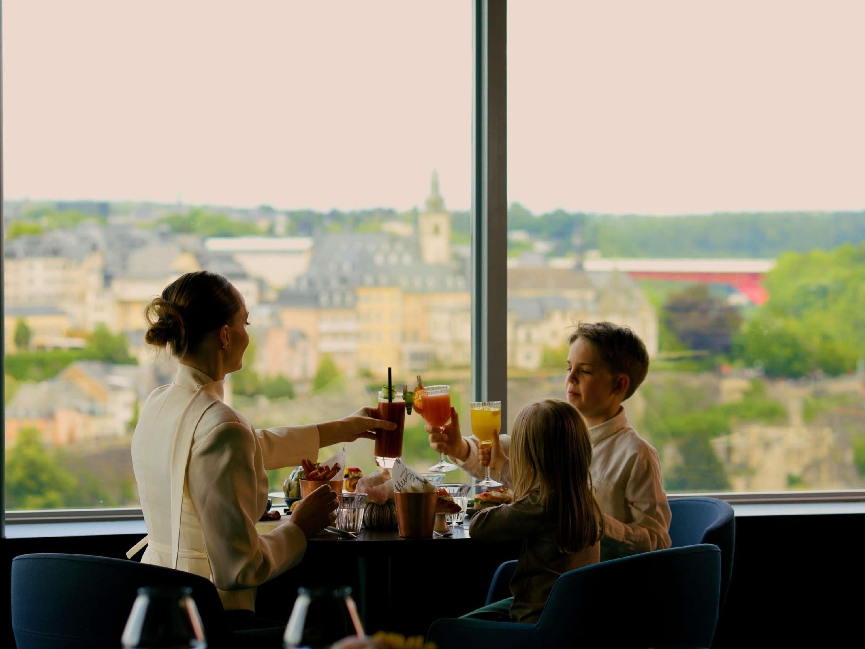 A dining area with a table set for three, overlooking a cityscape with buildings and greenery.